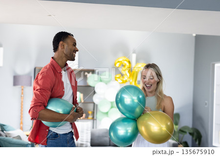 Celebrating birthday at home, friends holding colorful balloons and laughing together 135675910