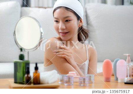 Beauty young asian woman applying cream or lotion while looking mirror in living room. Beauty young asian woman applying cream or lotion while looking mirror in living room. 135675917
