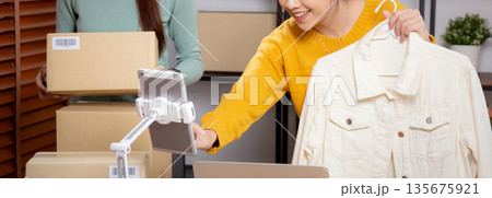 Two young asian woman live online clothing store while showing clothing with tablet and laptop. Two young asian woman live online clothing store while showing clothing with tablet and laptop. 135675921