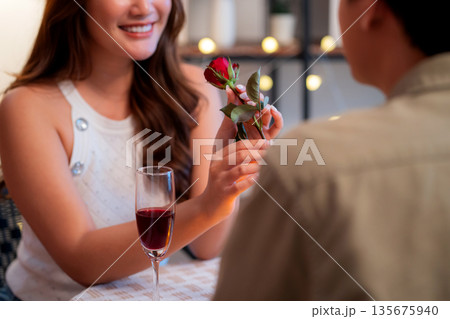 Romantic asian man giving rose to smiling woman during dinner, surprise gift for Valentine's Day. 135675940
