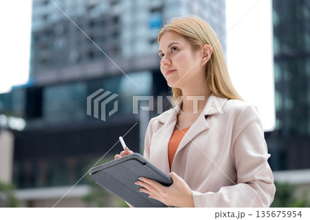 Young caucasian businesswoman writing on digital tablet in city. Young caucasian businesswoman writing on digital tablet in city. 135675954