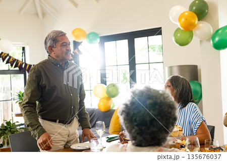 Elderly man standing and speaking at family gathering with festive balloons Elderly man standing and speaking at family gathering with festive balloons 135676037