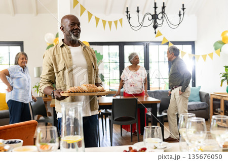 Elderly man serving bread at family gathering, smiling and enjoying celebration 135676050