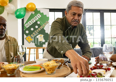 Man enjoying retirement party, reaching for snacks at festive gathering table Man enjoying retirement party, reaching for snacks at festive gathering table 135676051