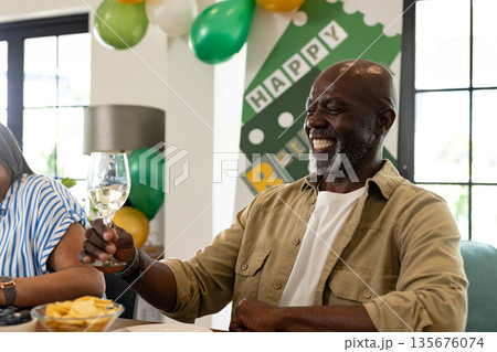 Smiling man raising glass at retirement party, celebrating joyful milestone indoors 135676074