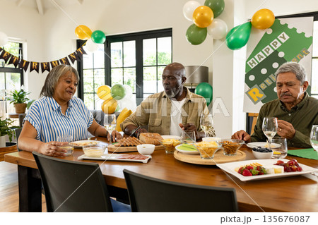 Celebrating retirement, diverse group sharing meal at home, smiling and talking 135676087