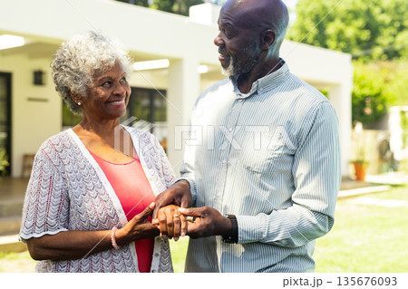Elderly couple holding hands and smiling warmly in sunny garden Elderly couple holding hands and smiling warmly in sunny garden 135676093