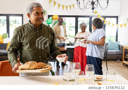 Smiling man serving bread and coffee at family gathering in cozy living room Smiling man serving bread and coffee at family gathering in cozy living room 135676112