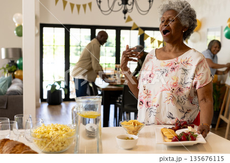 African American woman joyfully singing at family celebration with snacks on table African American woman joyfully singing at family celebration with snacks on table 135676115