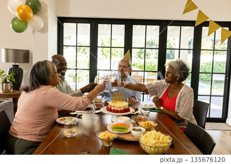 Toasting with drinks, African American friends celebrating birthday around decorated table 135676120