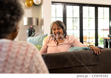 African American woman sitting on sofa at home, smiling and talking with friend 135676162