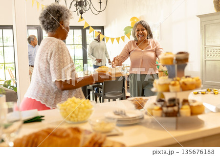 Smiling women enjoying pastries and conversation at home during festive gathering 135676188