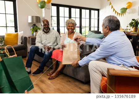 Elderly woman receiving gift bag, smiling joyfully with friends at home celebration Elderly woman receiving gift bag, smiling joyfully with friends at home celebration 135676189