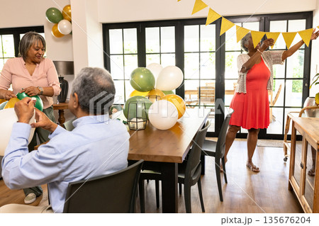 Senior friends hanging bunting and arranging balloons for celebration at home Senior friends hanging bunting and arranging balloons for celebration at home 135676204