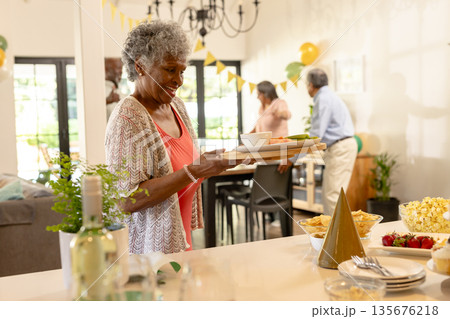 Elderly woman serving food at family gathering, smiling and enjoying celebration Elderly woman serving food at family gathering, smiling and enjoying celebration 135676218