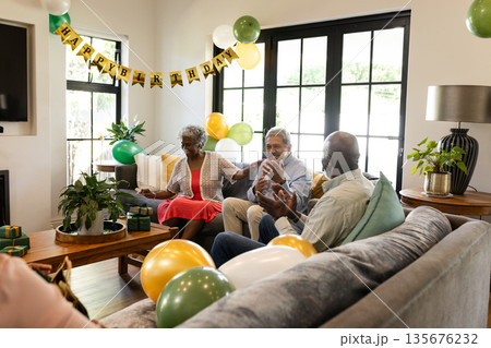 African American seniors celebrating birthday, having conversation in living room with balloons African American seniors celebrating birthday, having conversation in living room with balloons 135676232