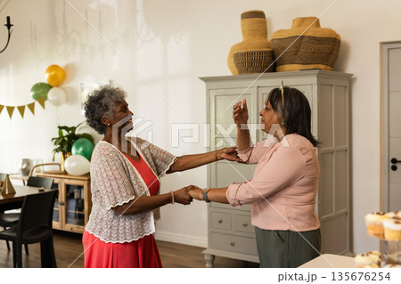 Two joyful women dancing together at home, celebrating with laughter and happiness Two joyful women dancing together at home, celebrating with laughter and happiness 135676254