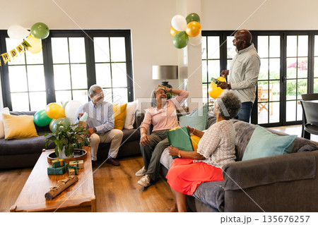 Friends laughing and celebrating birthday at home with balloons and gifts 135676257