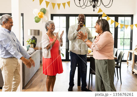 Group of friends laughing and clapping at home during festive celebration 135676261
