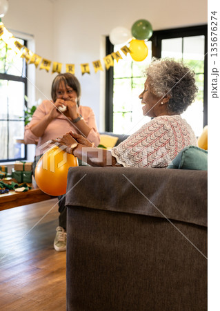 Elderly women enjoying birthday celebration at home with balloons and decorations Elderly women enjoying birthday celebration at home with balloons and decorations 135676274