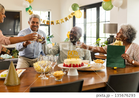 Family celebrating birthday with cake and gifts, raising glasses in living room Family celebrating birthday with cake and gifts, raising glasses in living room 135676293