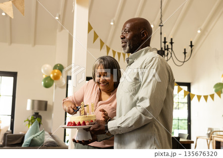 Smiling couple cutting birthday cake at home during festive celebration 135676320