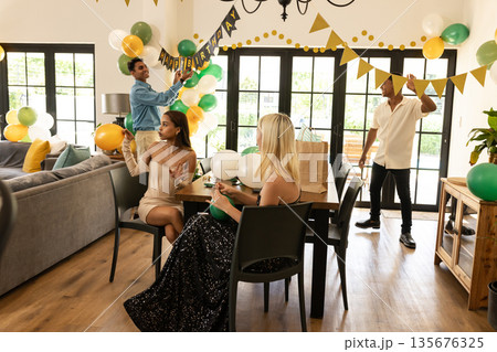 Arranging balloons and banners, diverse friends decorating for birthday party at home Arranging balloons and banners, diverse friends decorating for birthday party at home 135676325