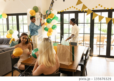 Friends decorating living room with balloons and banners for festive celebration Friends decorating living room with balloons and banners for festive celebration 135676329