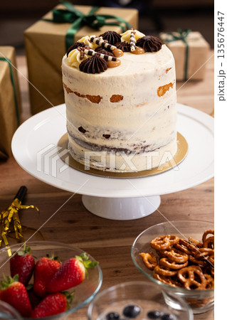 Tall cake with chocolate decorations on table surrounded by gifts and snacks Tall cake with chocolate decorations on table surrounded by gifts and snacks 135676447
