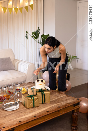Woman decorating cake with candles on wooden table during festive celebration Woman decorating cake with candles on wooden table during festive celebration 135676454