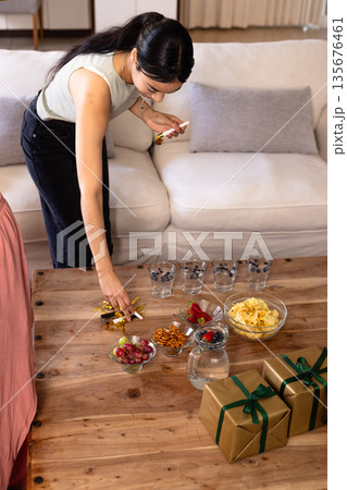 Woman arranging snacks and gifts on wooden table, preparing for celebration at home Woman arranging snacks and gifts on wooden table, preparing for celebration at home 135676461