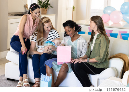Women celebrating baby shower at home, sharing gifts and joyful moments together Women celebrating baby shower at home, sharing gifts and joyful moments together 135676482