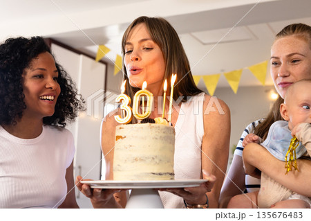 Blowing out candles, woman celebrating birthday with friends and baby at home Blowing out candles, woman celebrating birthday with friends and baby at home 135676483