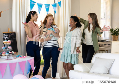 Women celebrating baby shower with cupcakes and decorations in cozy living room Women celebrating baby shower with cupcakes and decorations in cozy living room 135676486