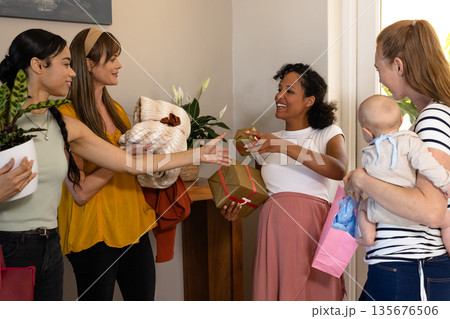 Women exchanging gifts and smiles at home during joyful celebration Women exchanging gifts and smiles at home during joyful celebration 135676506