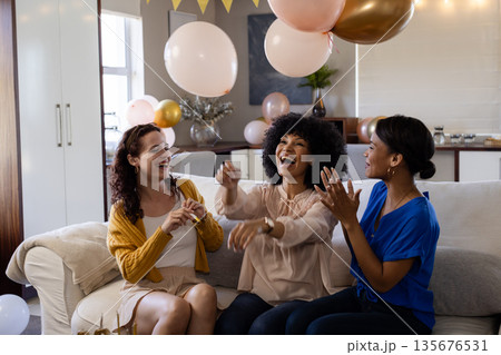 Women laughing and celebrating with balloons at home, enjoying festive atmosphere 135676531