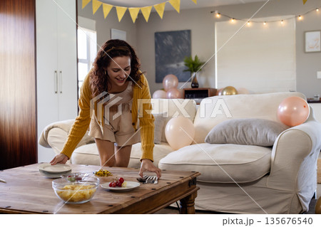Woman decorating living room table with snacks and balloons for celebration 135676540