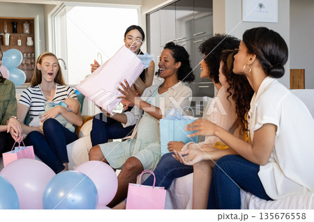 Women celebrating baby shower at home, opening gifts and enjoying together 135676558