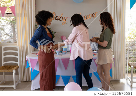 Friends celebrating baby shower, smiling and touching pregnant woman's belly at home Friends celebrating baby shower, smiling and touching pregnant woman's belly at home 135676581
