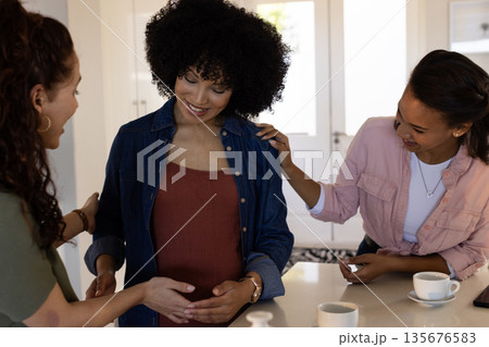 Friends celebrating pregnancy, smiling and touching belly at home with coffee cups Friends celebrating pregnancy, smiling and touching belly at home with coffee cups 135676583