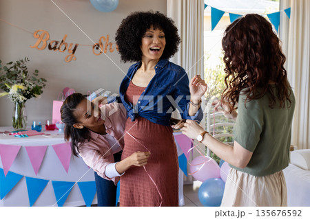 Celebrating baby shower, friends measuring mom-to-be's belly, smiling and laughing Celebrating baby shower, friends measuring mom-to-be's belly, smiling and laughing 135676592