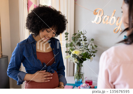 Pregnant woman smiling and touching belly at baby shower celebration indoors Pregnant woman smiling and touching belly at baby shower celebration indoors 135676595