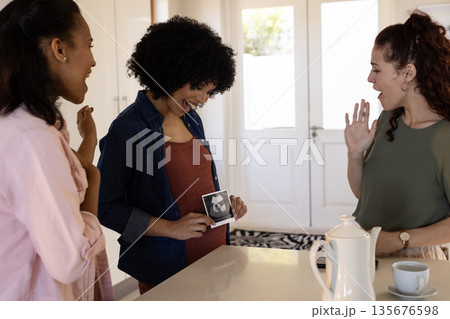 Celebrating pregnancy announcement, friends in cozy kitchen with ultrasound picture Celebrating pregnancy announcement, friends in cozy kitchen with ultrasound picture 135676598