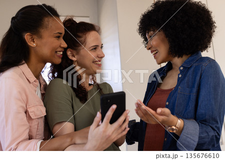 Celebrating together, friends sharing joyful moments with smartphone in living room Celebrating together, friends sharing joyful moments with smartphone in living room 135676610