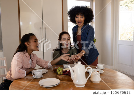 Women enjoying tea and snacks at home, sharing laughter and conversation Women enjoying tea and snacks at home, sharing laughter and conversation 135676612