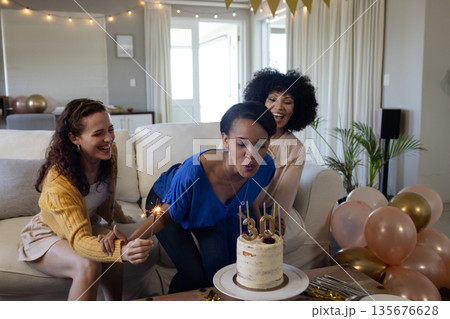 Celebrating birthday, woman blowing candles on cake with friends at home Celebrating birthday, woman blowing candles on cake with friends at home 135676628
