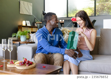 Couple exchanging gifts on sofa at home, celebrating special occasion together 135676652