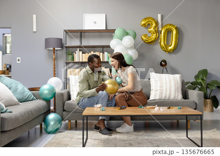 Couple celebrating 30th birthday at home, surrounded by balloons and decorations Couple celebrating 30th birthday at home, surrounded by balloons and decorations 135676665