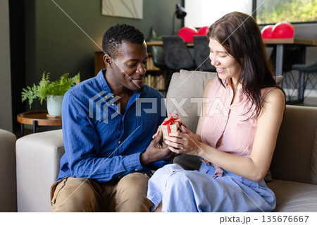 Couple exchanging gift on sofa, smiling and enjoying special moment together 135676667