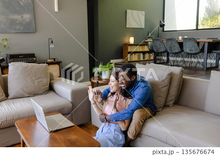Couple sitting on couch video chatting with friends on laptop at home Couple sitting on couch video chatting with friends on laptop at home 135676674